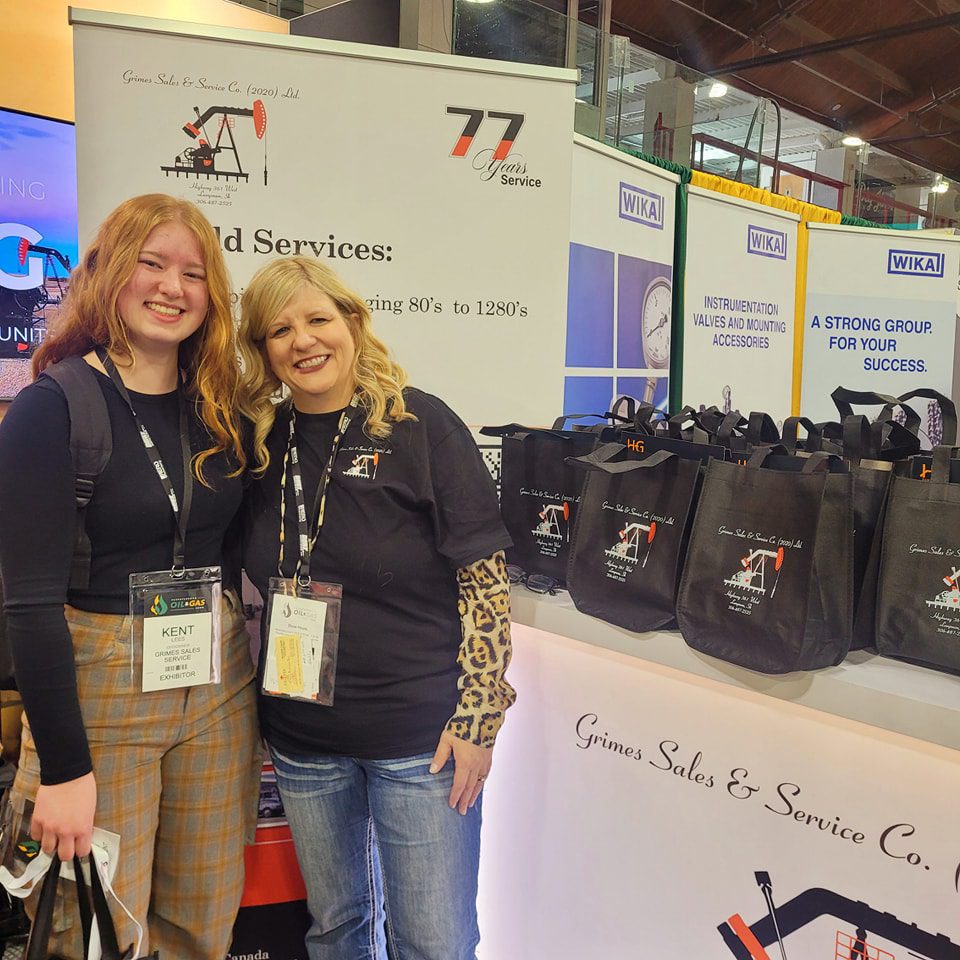 Two women standing side by side, engaged in conversation at a bustling trade show event.